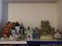 Wide shelf view showing all seven porcelain houses together, arranged side by side with size ranging from small to taller multi-story buildings