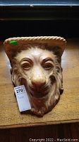 Front view of ceramic lion sconce showing detailed lion face and braided border with a tag indicating it is a sconce and lot number 270.