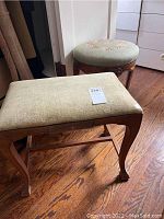 Two upholstered wooden stools on wooden floor. Rectangular stool with beige upholstery and round stool with floral green upholstery.
