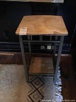 Full view of the small square table with a metal frame, top onyx surface, and bottom onyx shelf, placed on a rug.