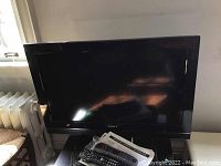 Full front view of the Sony Bravia TV showing screen, stand, remote control and manuals on table beneath the TV.