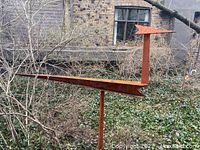 Full view of rust-colored geometric bird silhouette mounted on vertical stake in garden