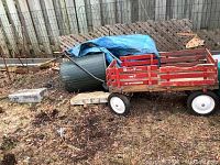 Full side view of the red Berlin Flyer wood wagon with sides; weathered outdoor surroundings visible.