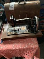 Image showing the full sewing machine with wooden case in the background on a textured cloth surface.
