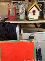 Two bird houses, a red metal and glass candle lantern, and a wood-framed sandwich board sign on shelf.