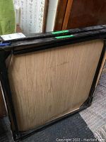 Table folded flat showing the underside wood panel and black metal frame