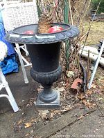 Full view of the black cast iron planter with pine cone and faux apples inside, showing outdoor placement and condition.