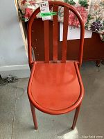 Front view of red powder coated metal chair with three metal back slats, one bent, all painted red.