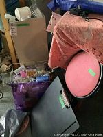 Photo showing the pink folding stool, travel poncho in bag, craft bottles in basket, and other containers on a shelf