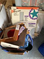 Photo showing boxed 3-piece cutting center, wooden frames, fabric scraps, and various craft supplies packed in a blue container.