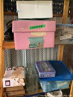 Photo showing stacked boxes including a pink quilt project box labeled 11x17, clear glass vases, Valency home hair remover system box, a decorative tin box, and a plastic container labeled 'Matter'