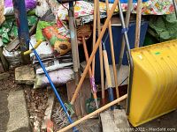 Shot showing multiple garden tools including snow shovels, rake aerator, and various shovels leaning against a wall with bags in background.