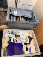 Two gray plastic bins, one with full sheets of glass and one with offcuts, tools, patterns and bottles