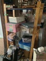 Wooden four-shelf IKEA shelving unit holding multiple storage boxes and items, showing structural wear and a need for tightening.