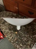 White metal hanging light shade with attached chain and power cord, shown on a patterned surface in an interior setting.