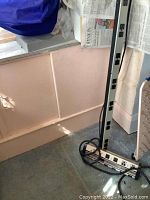 Long vertical power bar standing upright near a window with thick black cable coiled at the base.