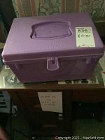 Purple plastic box with lid closed showing latch and handle, placed on wooden surface with MaxSold sticker visible