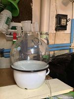 White enamel chamber pot holding round Chemiglass container with multiple neck openings shown in basement setting.