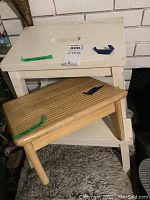 Photo showing two wooden stools stacked: a white painted wooden stool with handle cutout on the top and a natural wood footstool with grooved surface.