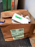 Opened cardboard box containing loose white ceramic subway tiles labeled 3x6 on green tape.