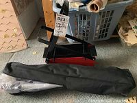 Photo showing a red metal brazier with black handles and a black nylon carrying case containing a tripod.