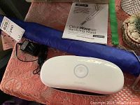 Photo showing white 59S sterilizing box with circular power button and power adapter on pink fabric surface. Instruction manual for Verilux CleanWave Wand also visible.