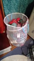 Mesh laundry hamper filled with assorted yarn balls and skeins in various colors.