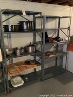 Full view of two grey metal shelving units loaded with kitchen pots, pans, and some miscellaneous items, showing overall structure and shelf spacing.