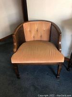 Front view of one vintage wooden chair with tan upholstered seat and button-tufted back cushion, curved wooden frame and woven cane sides.