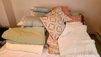 Stack of assorted blankets and pillows with different colors and patterns, showing texture and variety.