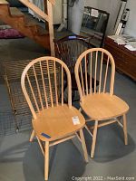 Photo showing two matching light-colored wooden chairs, one vintage dark wood chair, and a metal vintage style rolling rack on caster wheels in a basement setting.