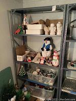 Wide view of metal shelving with multiple Christmas decorations including figurines, storage bins with ornaments, and tins