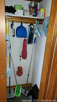Cleaning supplies including mops, dusters, broom, dustpan, hangers and stool stored in closet