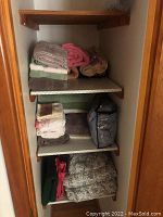 View of three shelves with neatly folded towels and bedding sets including floral patterns in storage bags