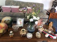 Overall view of decorative plates, figurines, cut glass vase with artificial flowers, small ceramic candy dish, and vintage Mickey Mouse figurine on table in living room.