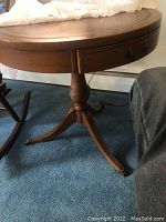 Wooden drum table with a lace doily on top and blue carpet floor, side angle