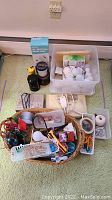 Photo shows assorted hand tools, office supplies, cords, scissors, magnets, stained glass charms, untested light bulbs in plastic bin and organizers.