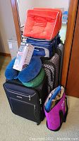 Photo shows stacked travel items including 2 suitcases, 2 travel neck pillows, a cooler bag, travel wedge pillow, and tote bags.