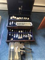 Full view of Rogers Bros. silverplate flatware set inside a wooden box with a closed upper compartment and open bottom drawer on carpet floor.
