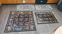 View of all four rugs and mats on wood floor, two square floral rugs, two rectangular patterned mats