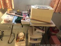 Overall view of sewing machine in case on table with multiple containers of sewing supplies and a wooden ruler lying on top.