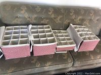 Four pink fabric storage boxes with grid dividers containing multiple stemware glasses shown on a couch.