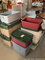 Multiple plastic storage bins stacked in a basement setting, showing variety of sizes and colors.