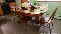 Full dining table with four chairs around it, table decorated with various household items.