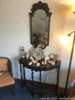 Console table with decorative items underneath ornate wall mirror, showing overall setup and condition.