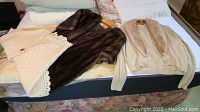 Three vintage fashion items laid out: white crochet shawl, dark brown fur wrap, beige cashmere sweater with fur collar.