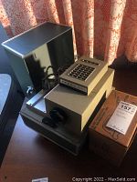 Full view of Argus 500 projector with attached power cord and original box.