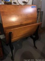 Vintage wooden school desk with hinged top and black cast iron legs, shown folded upright.