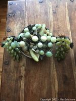 Top-down view of the fruit basket with carved hard-stone grapes, pears, apples, bananas in brass bowl on wood table