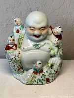 Front view of porcelain Buddha figure with five children, showing detailed hand-painted colors and facial expressions.